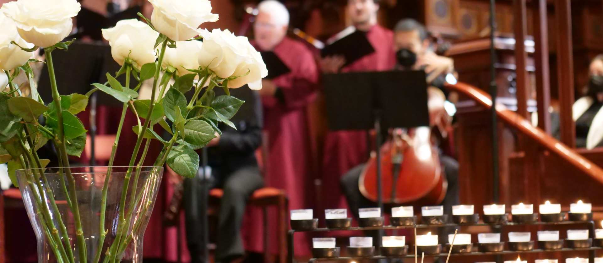 White roses and candles in front of a cello player and singers.