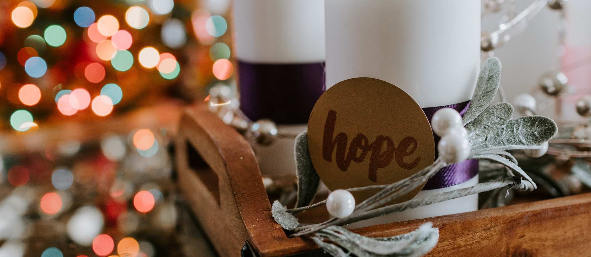 Two advent candles, one labeled "hope", with a Christmas tree in the background.